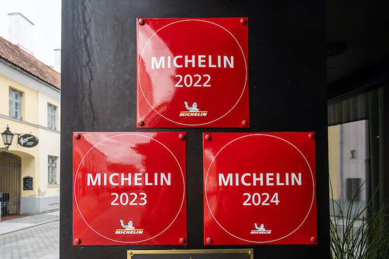 Three square red signs read _Michelin 2022_ _Michelin 2023_ and _Michelin 2024_ on a restaurant door frame. 768.jpeg